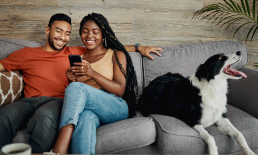 Couple sitting on couch with dog checking their phone.