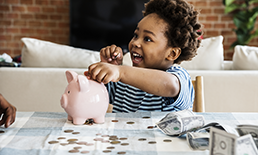 Child putting money in a piggy bank.