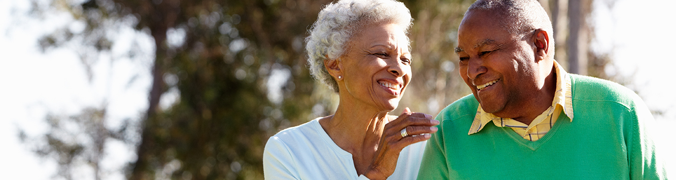 Two senior citizens, a man and a woman, laughing toward each other while walking outside.