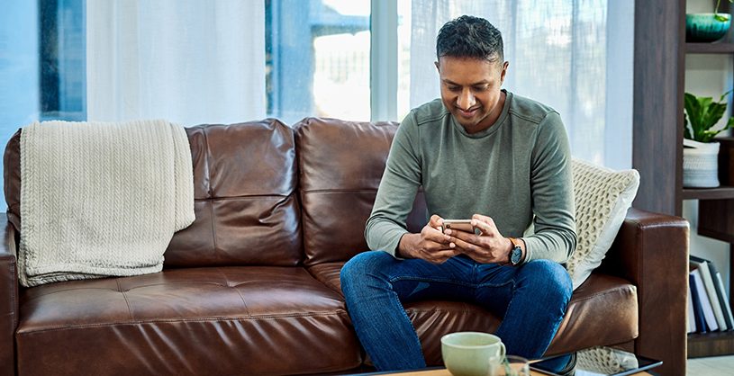 man sitting on a couch looking at a mobile device