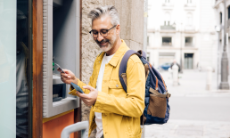 Man checking phone while using an ATM traveling abroad
