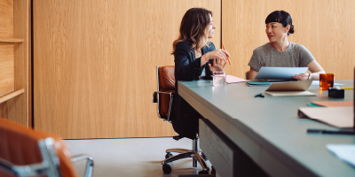 Two women meeting in a wood-paneled conference room at the end of a table