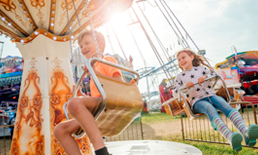 Two children on the swings at an amusement park.