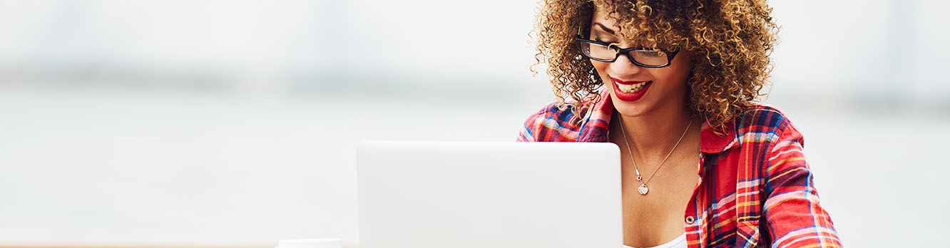 A woman in glasses smiling while looking at her laptop