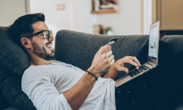 Man on laptop computer viewing finances holding credit card.