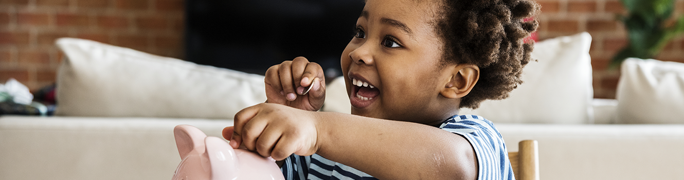 child putting money in a piggy bank