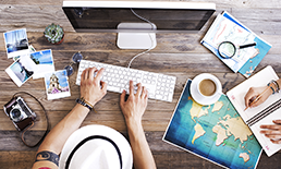 Person typing on a computer while looking at travel maps.