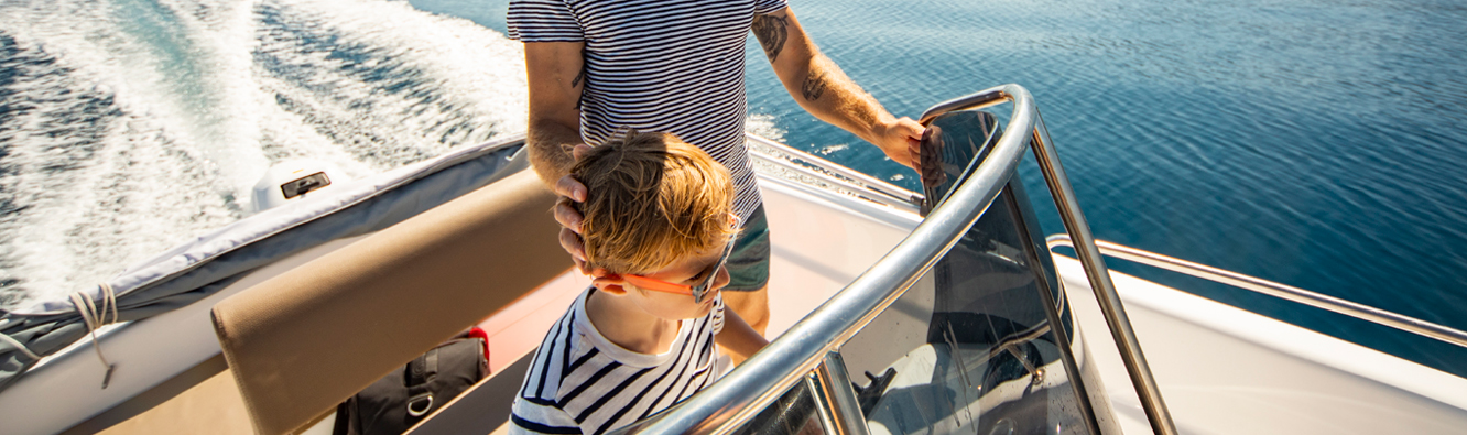 Happy father and son driving a boat on the open water.