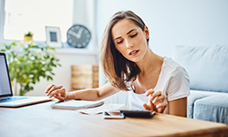 Woman sitting at a desk with her laptop while using a calculator