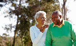 Two senior citizens, a man and a woman, laughing toward each other while walking outside.