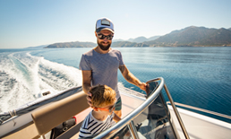 Happy father and son driving a boat on the open water.