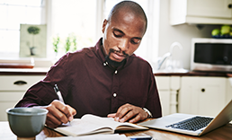 man looking at a computer and taking notes