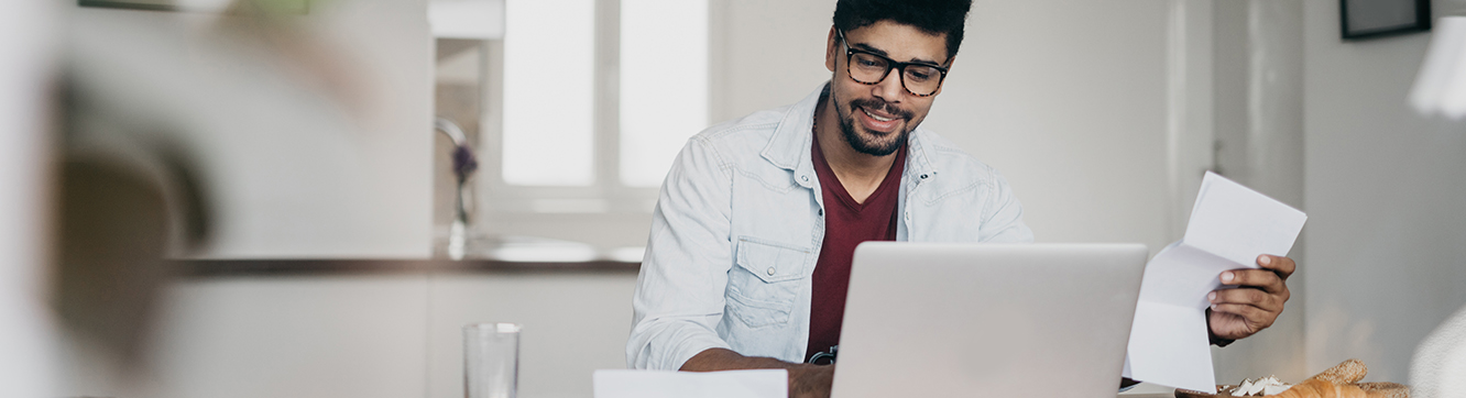 man holding paper looking at computer