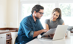 couple sitting at kitchen table looking at a paper with laptop open