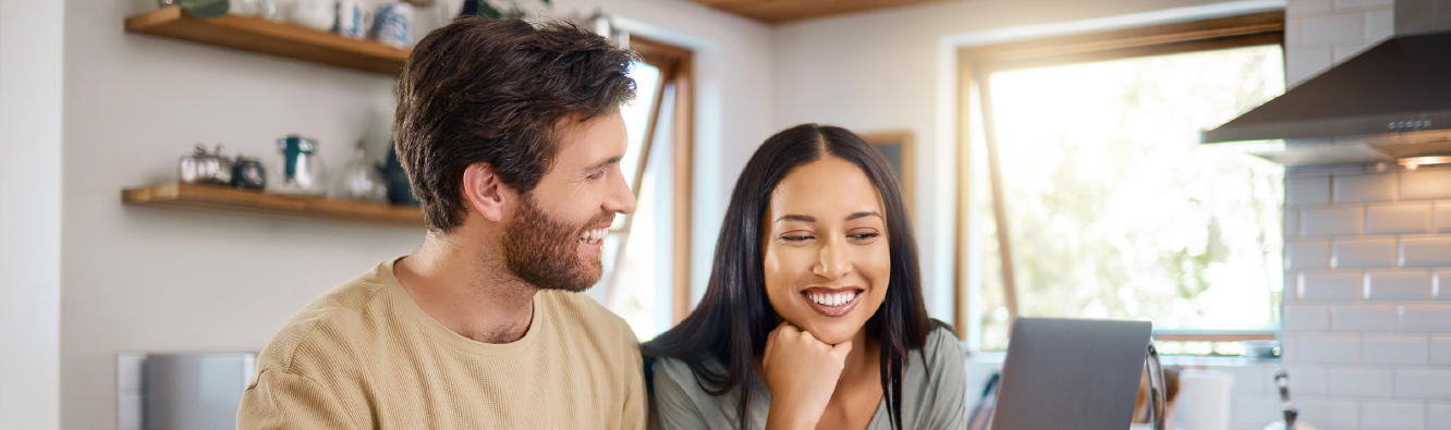 Man and woman sitting in kitchen working on laptop together