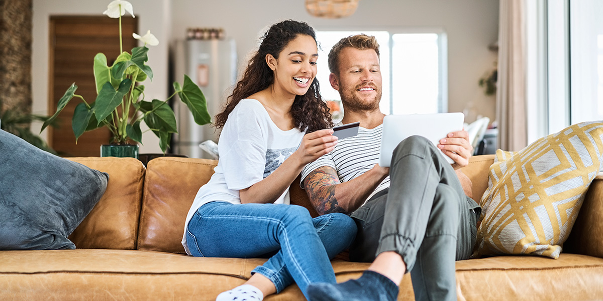 couple sitting on couch looking at card and mobile device