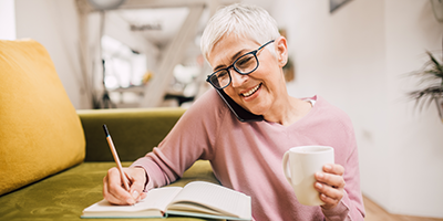 woman on the phone holding a coffee mug and writing notes