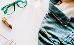 Denim jacket, lipstick, glasses flatlay.