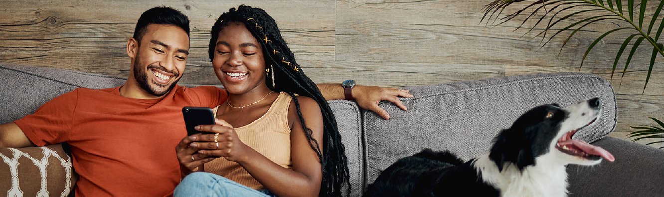 Couple sitting on couch with dog checking their phone.