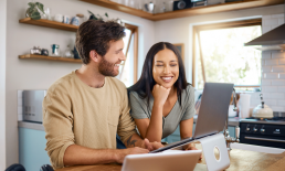 Man and woman sitting in kitchen working on laptop together