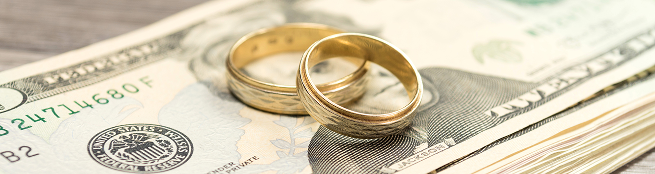 Stack of $20 bills with two wedding bands on top.