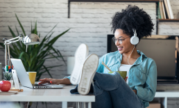 Woman with headphones looking at laptop with feet on desk