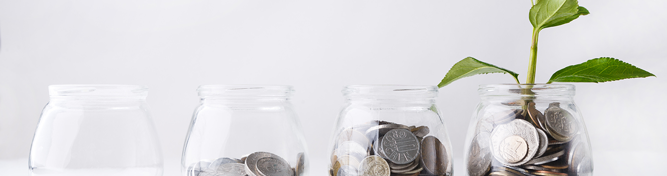 Four glass jars filled with increasing amount of change with rightmost jar sprouting a plant