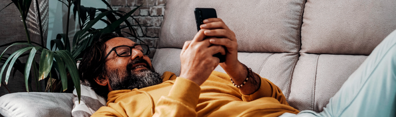 Man smiling laying on couch using his smartphone.