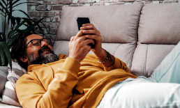Man smiling laying on couch using his smartphone.